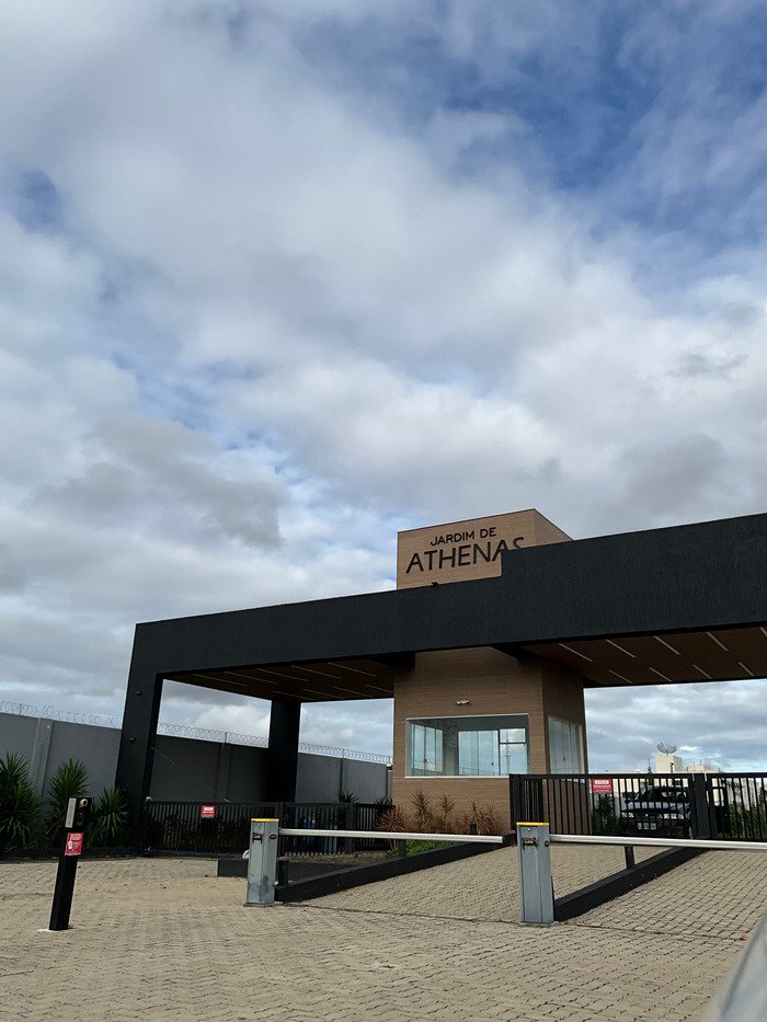 Fachada moderna da portaria do Condomínio Jardim de Athenas, em Campos dos Goytacazes, com estrutura de segurança e paisagismo.